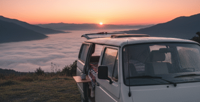 Furgoneta camper aparcada de frente, con la puerta trasera abierta, mirando hacia un espectacular amanecer sobre un mar de nubes en un valle gallego.